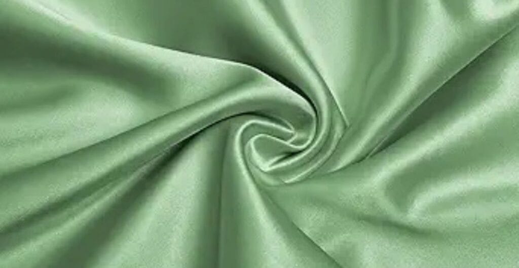 Light green satin fabric with a smooth, shiny texture, gathered in a swirl pattern.