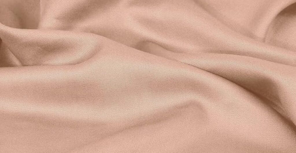 Close-up of a smooth, blush pink satin fabric with gentle folds and a soft sheen.