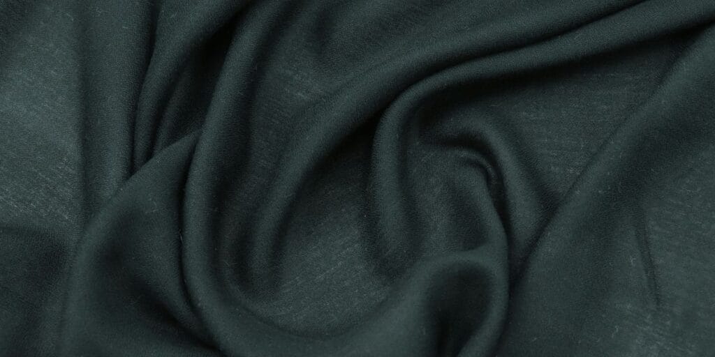 Close-up of dark green fabric with soft folds and a smooth texture.