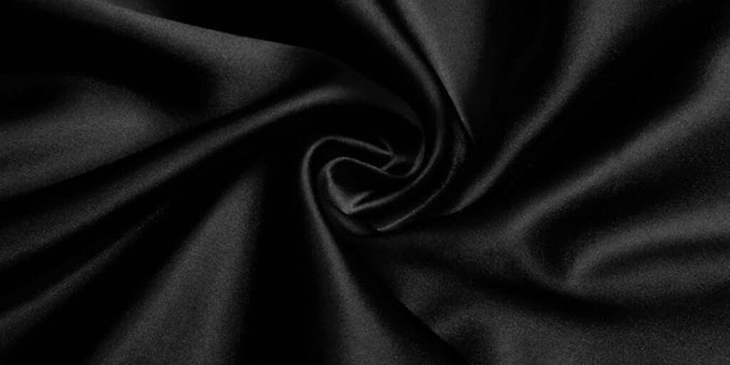 Close-up of smooth, black satin fabric with elegant folds and a central swirl pattern.