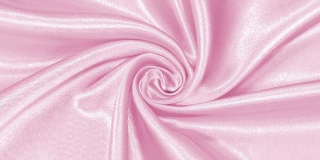 Close-up of shiny light pink satin fabric twisted into a swirl pattern.