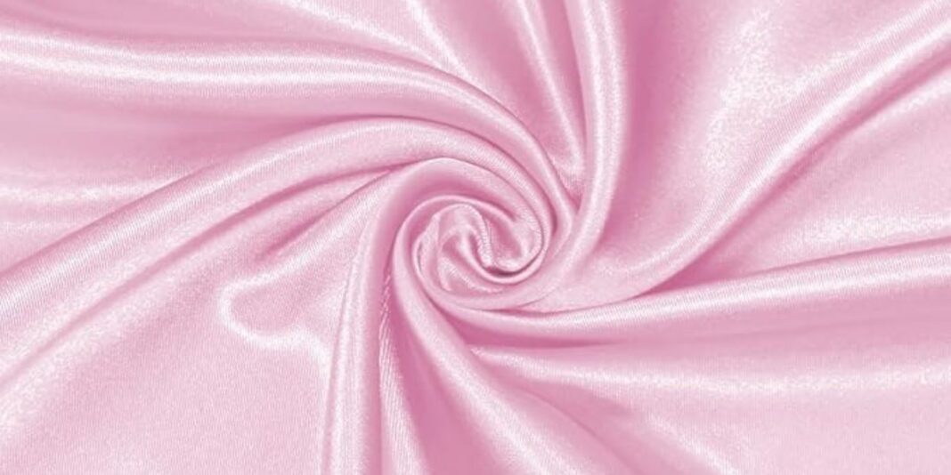 Close-up of shiny light pink satin fabric twisted into a swirl pattern.