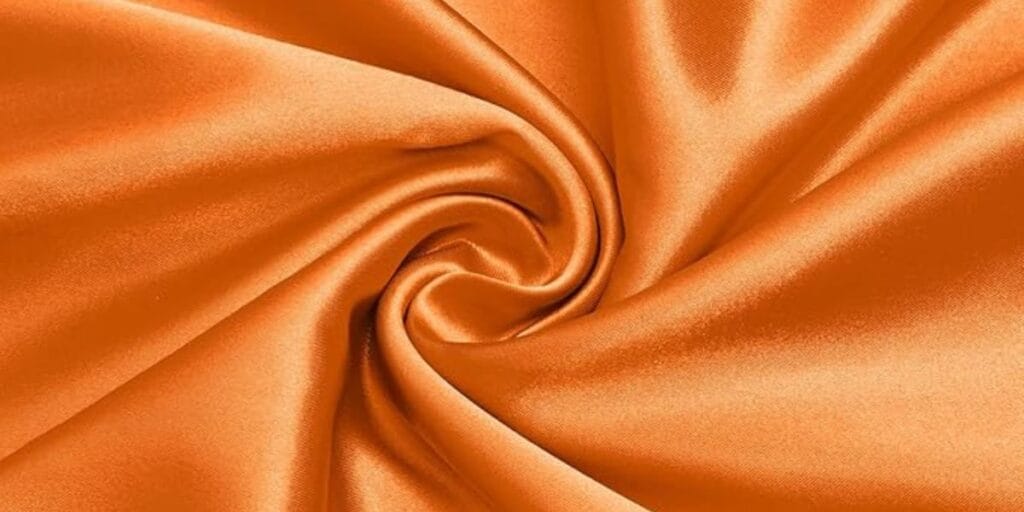 Close-up of smooth, orange satin fabric twisted into a swirl pattern.