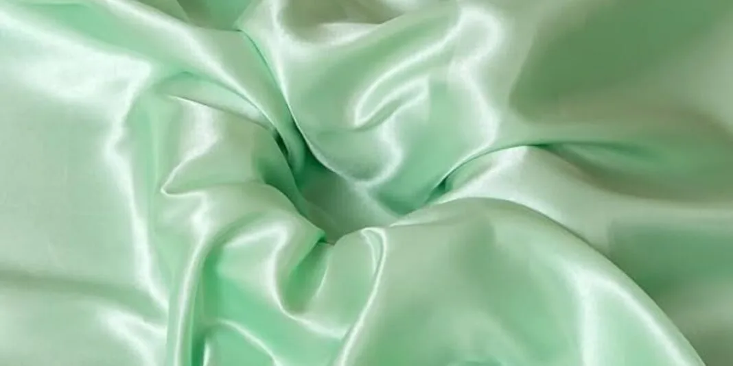 Close-up of light green satin fabric with smooth, shiny folds
