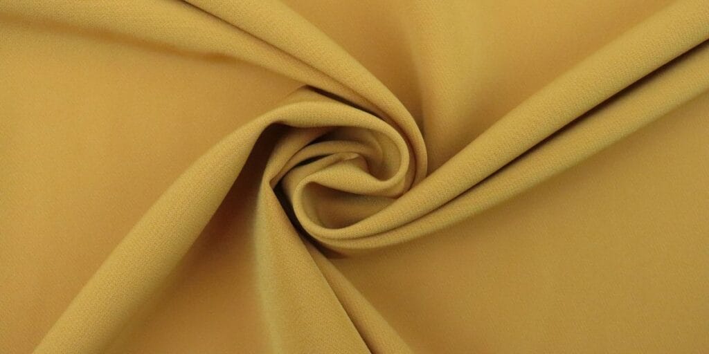 Close-up of mustard yellow fabric with a soft texture, twisted into a swirl.
