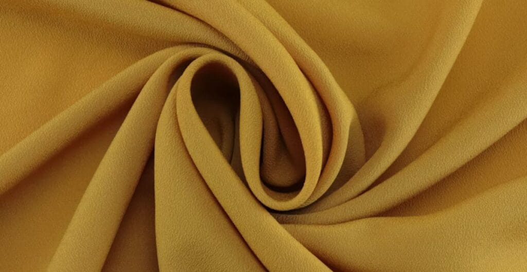 Close-up of mustard yellow crepe fabric with a soft, textured surface and elegant folds.