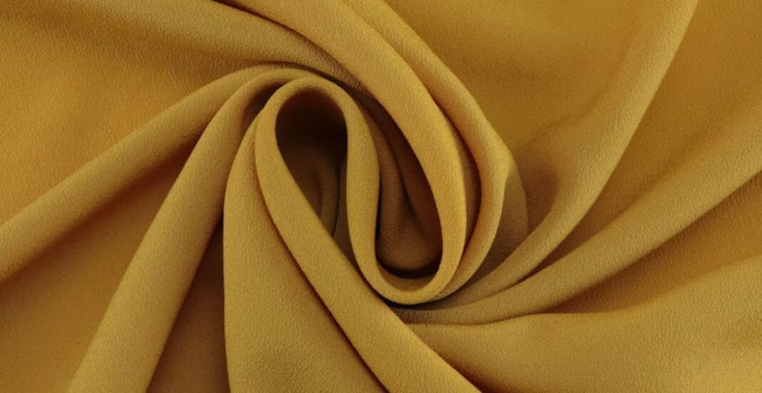 Close-up of mustard yellow crepe fabric with a soft, textured surface and elegant folds.