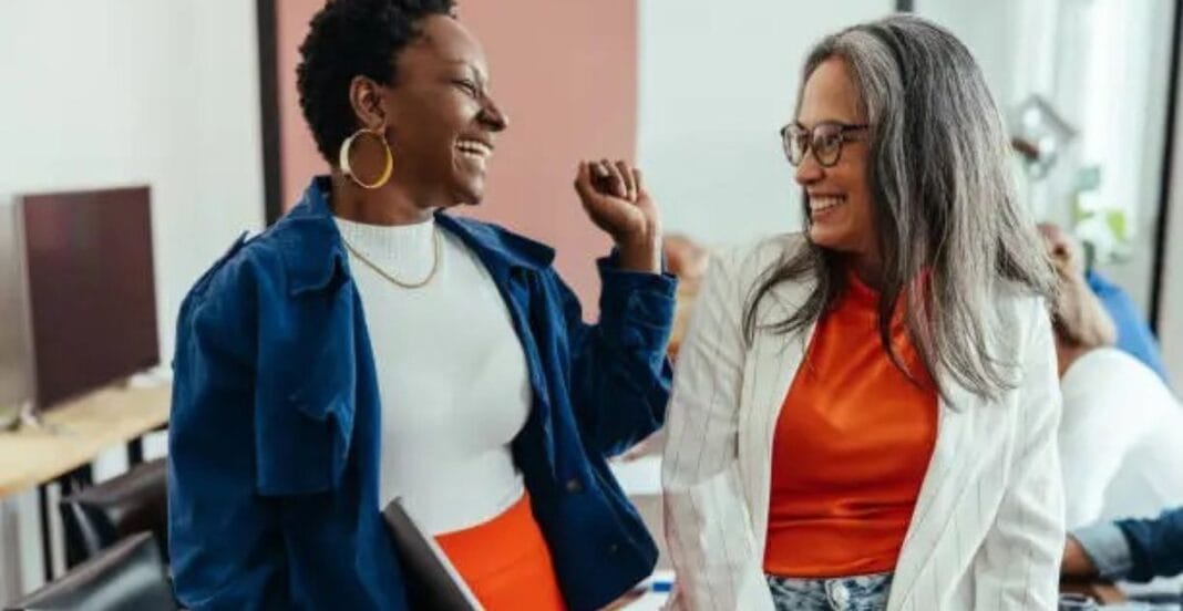 Two diverse women smiling and laughing together in an office setting.