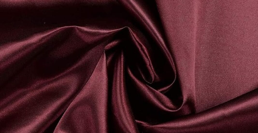 Close-up of smooth, shiny burgundy satin fabric with soft folds and a swirl in the center.