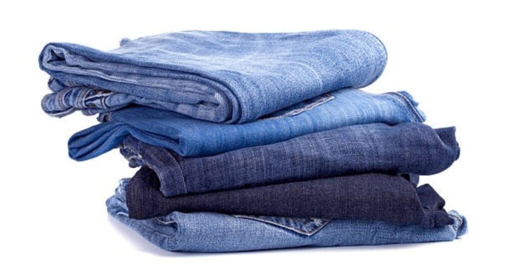 A stack of five folded denim jeans in various shades of blue.