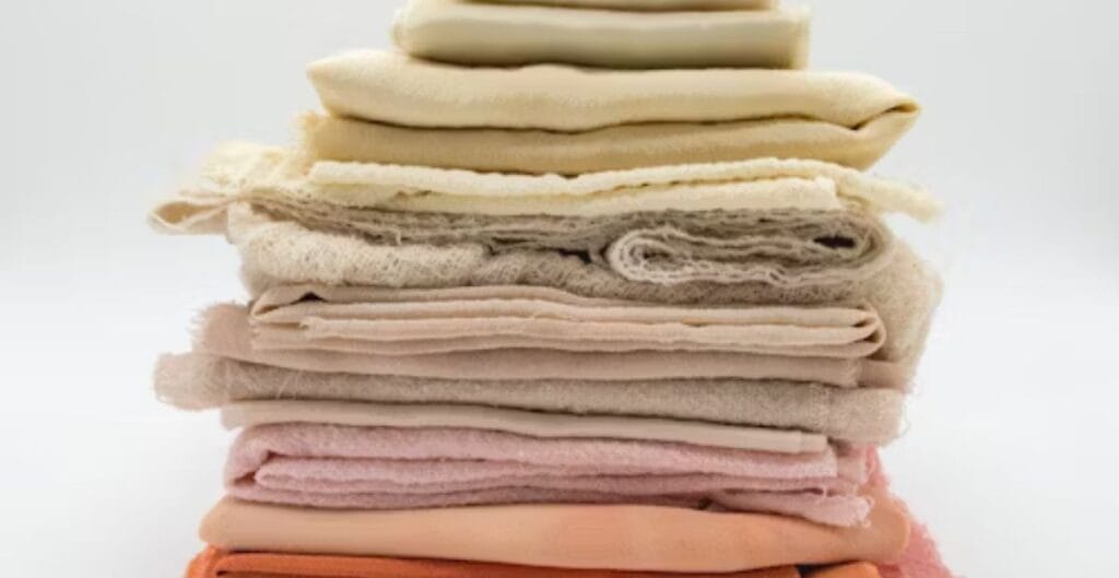 Stack of folded pastel-colored fabric in shades of cream, beige, pink, and orange.