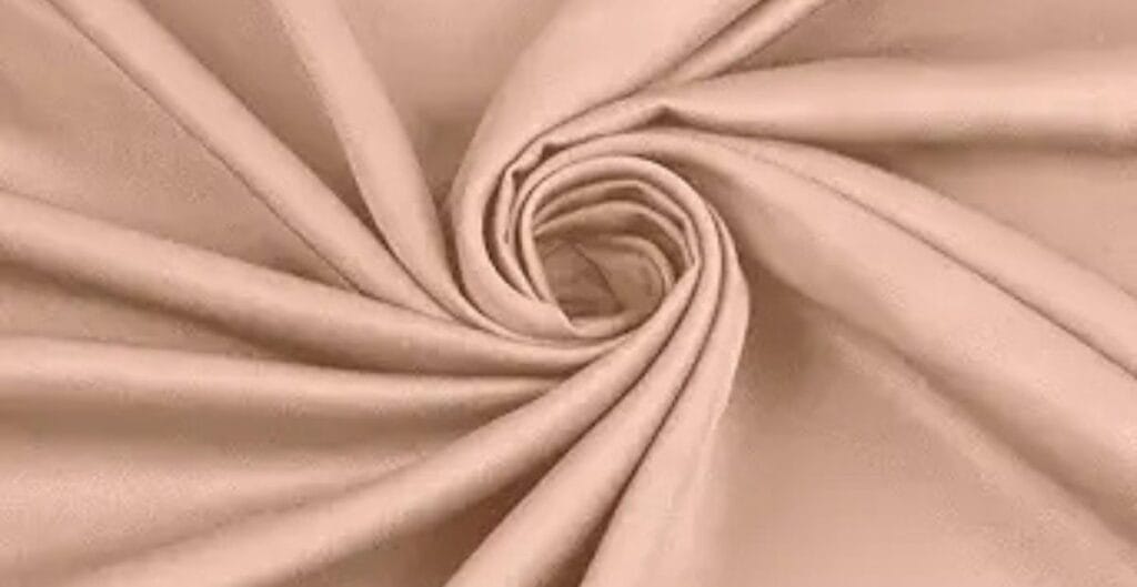 Close-up of beige fabric twisted in a spiral pattern, showcasing its soft and smooth texture.