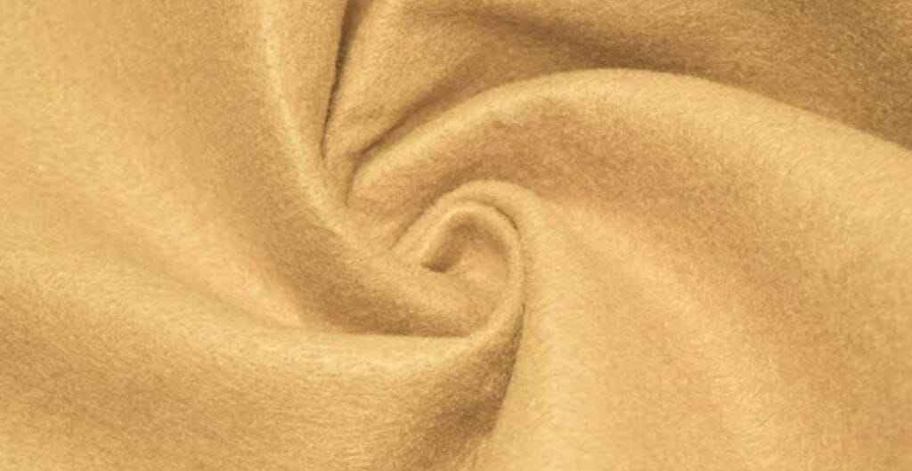 Close-up of light brown wool fabric with a soft, fuzzy texture and a twisted fold pattern.