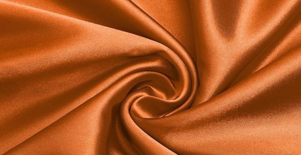 Close-up of smooth, shiny orange satin fabric twisted into a spiral pattern.