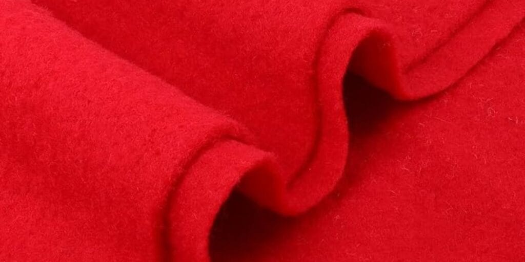 Close-up view of a bright red wool fabric with a soft and slightly fuzzy texture, folded in layers.