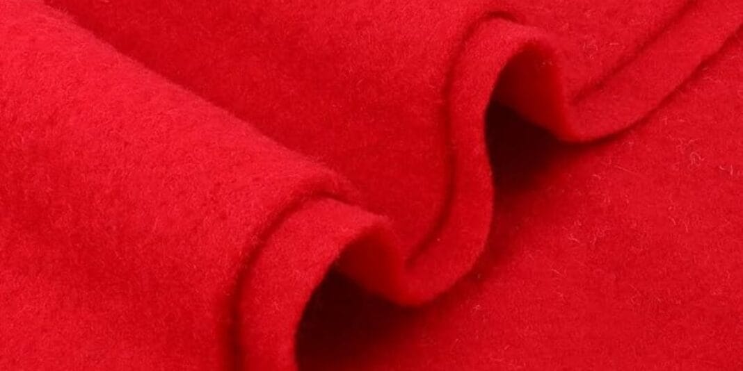Close-up view of a bright red wool fabric with a soft and slightly fuzzy texture, folded in layers.