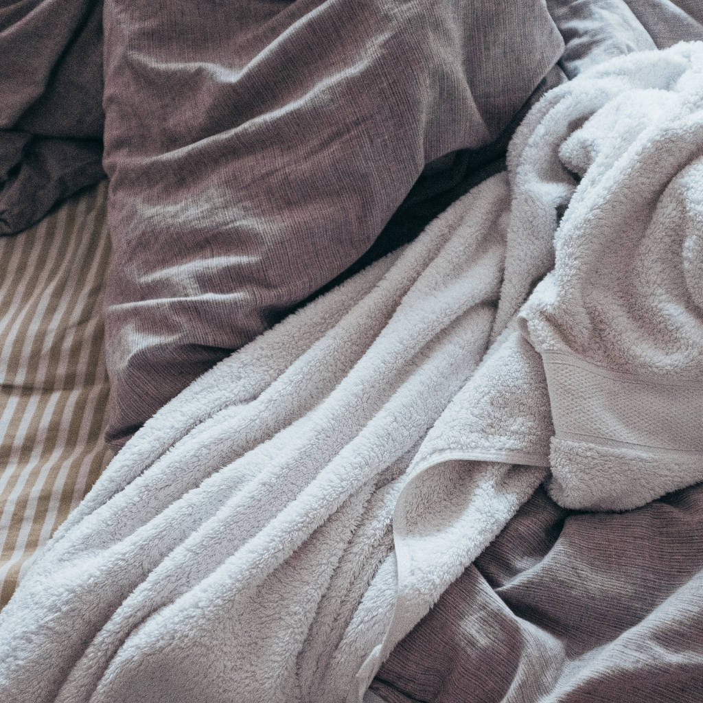 Close-up of a bed with a brown, textured blanket, a white towel, and striped bedsheets.