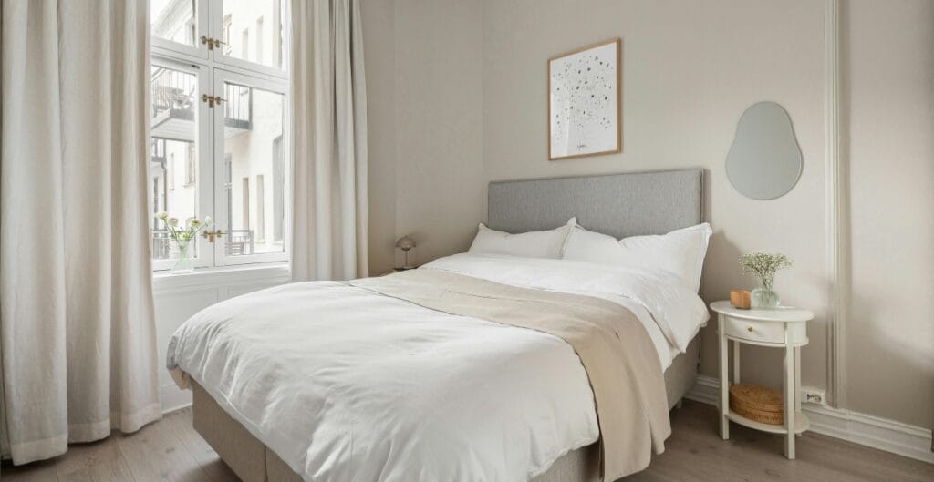 White linen curtains softly framing a sunlit bedroom window with minimalist decor.
