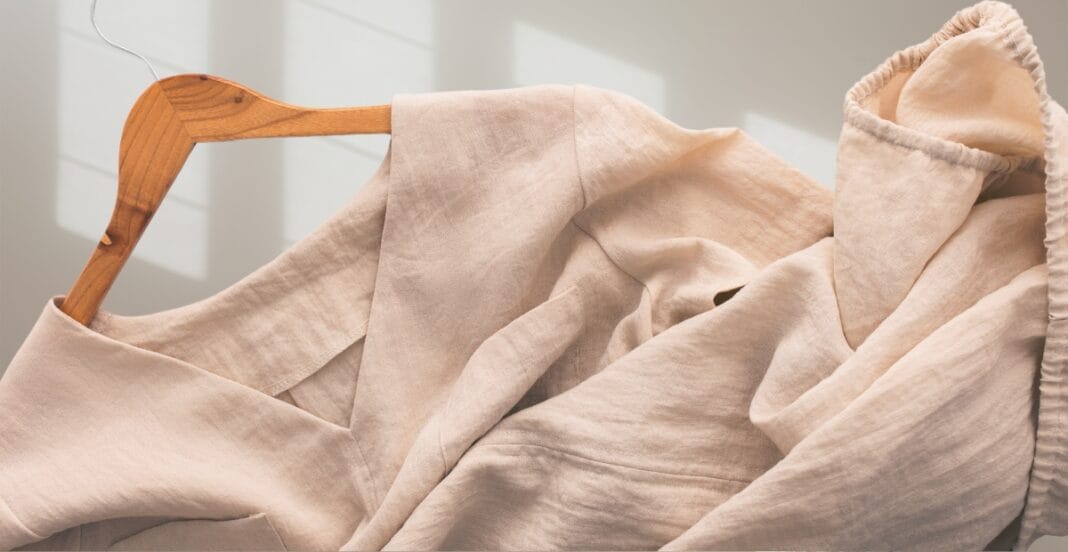 A beige linen shirt hanging on a wooden hanger against a white background.