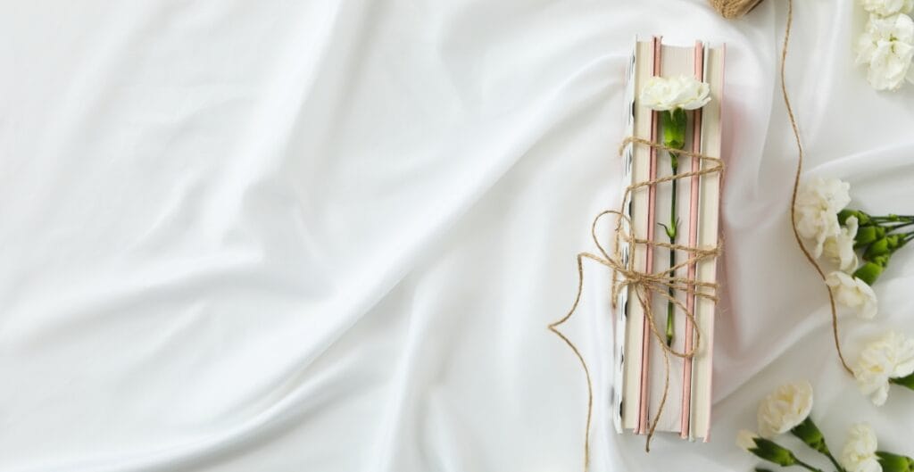 Elegant white fabric with a bundle of pink and white striped paper straws tied with twine, surrounded by white flowers.