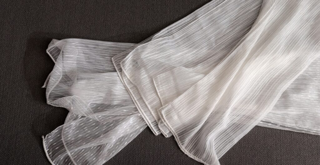 White sheer fabric with thin vertical stripes laid out on a dark surface.