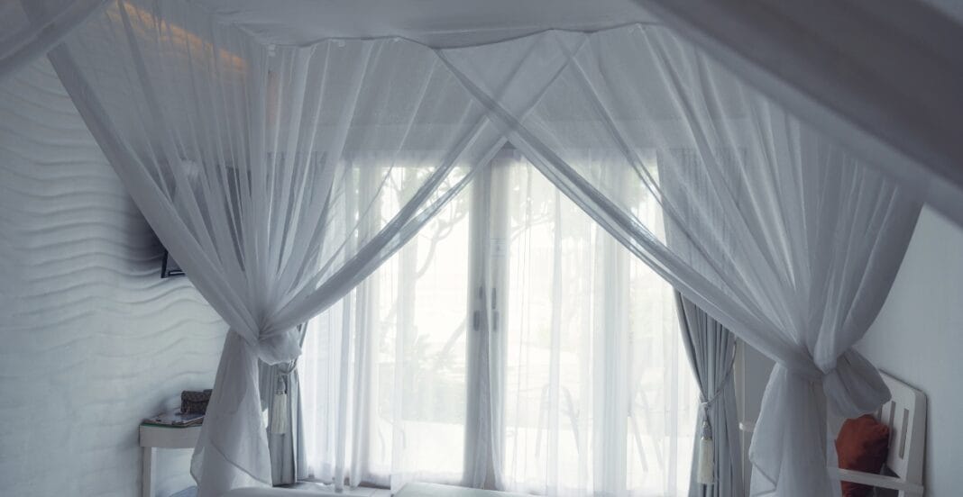 A bedroom with white curtains and sheer drapes hanging over large windows, allowing natural light to fill the space.