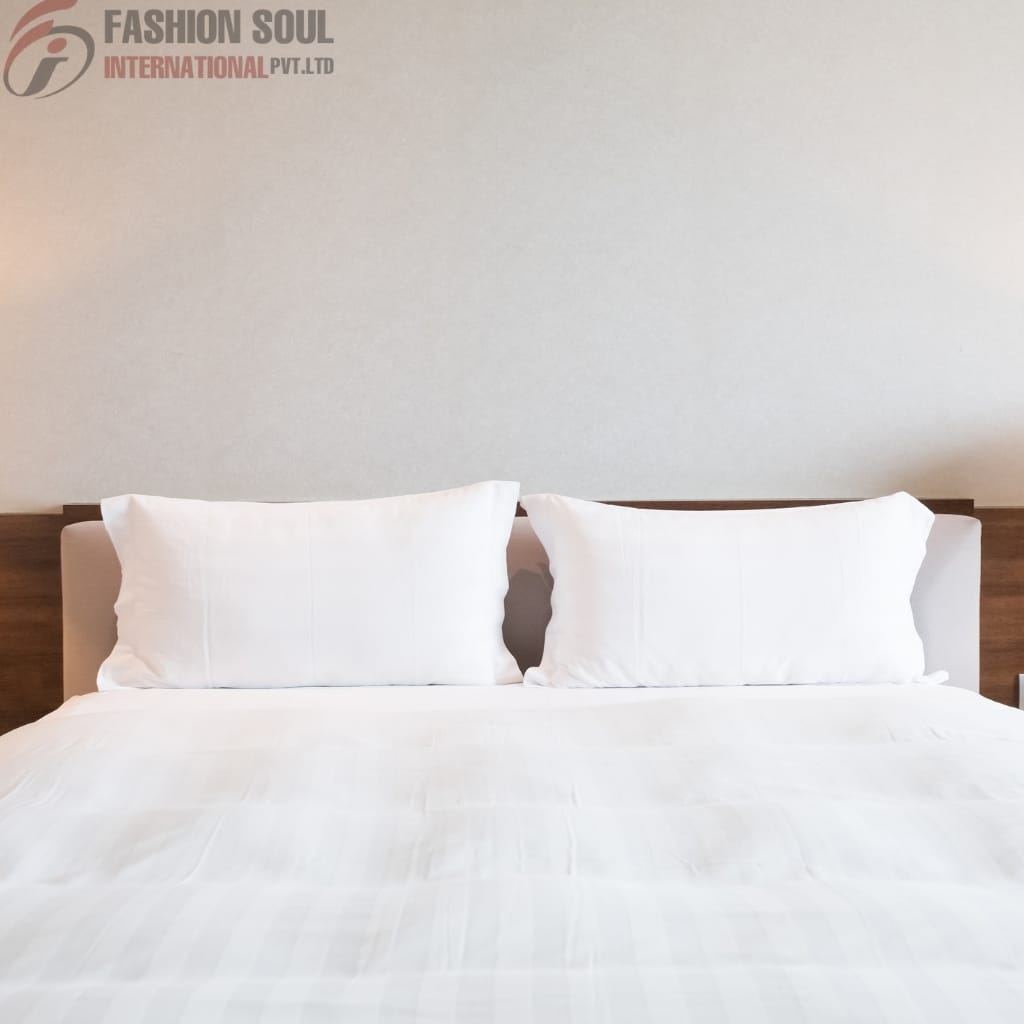 A neatly made bed with white pillows and white bedsheets, set against a plain light-colored wall with a wooden headboard.
