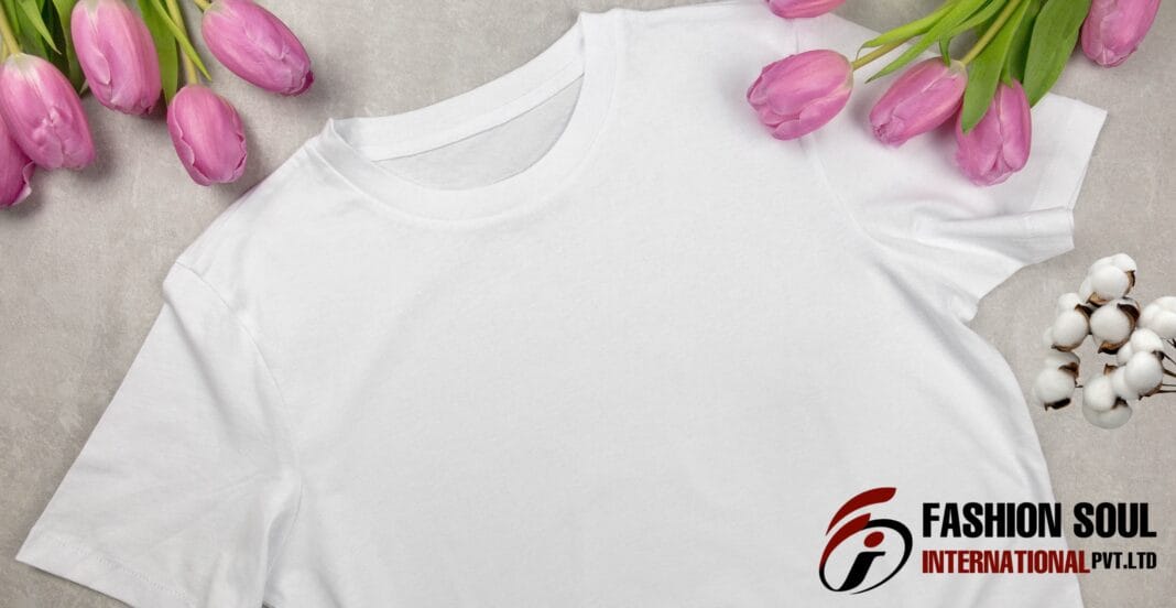 A plain white T-shirt laid flat on a grey surface, surrounded by pink tulips on the top left and right sides, and white cotton flowers on the right. The bottom right corner features a logo with the text 
