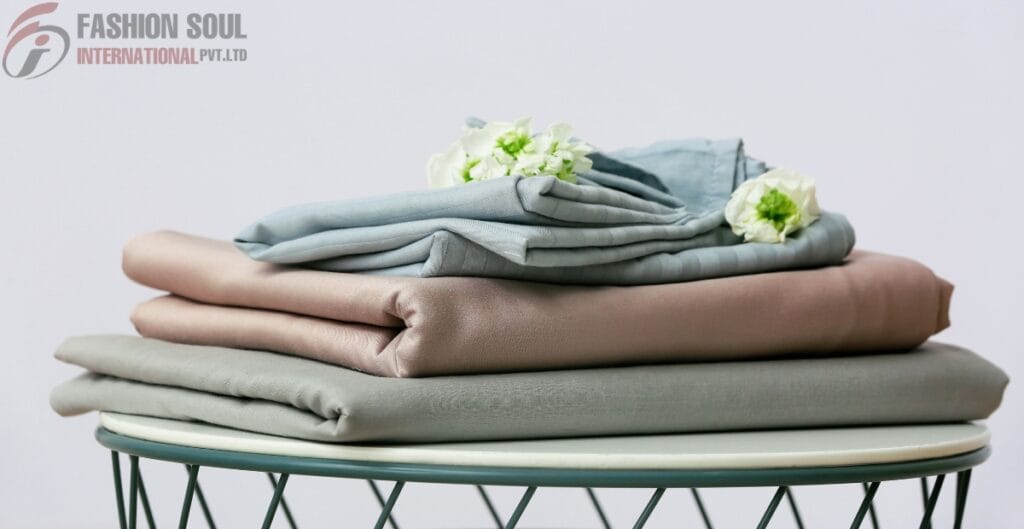 Stack of neatly folded pastel bed sheet bundles with flowers on top, displayed on a modern round table.