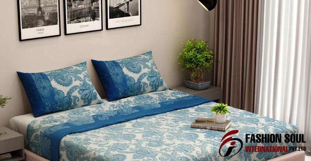 A neatly made bed with blue and white patterned bedspread and pillows in a modern bedroom. There are framed monochrome cityscape photos on the wall above the bed, a potted plant on the nightstand, and beige curtains covering a window to the right.