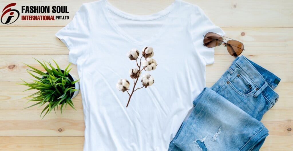 A flat lay of a white T-shirt with a cotton branch print, paired with ripped blue jeans, sunglasses, and a small green potted plant on a light wooden surface.