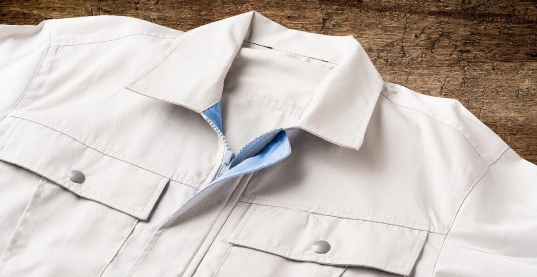 A close-up of a white Western-style jacket with snap buttons, lying on a wooden surface. The jacket has epaulets on the shoulders and a concealed zipper underneath the front flap.