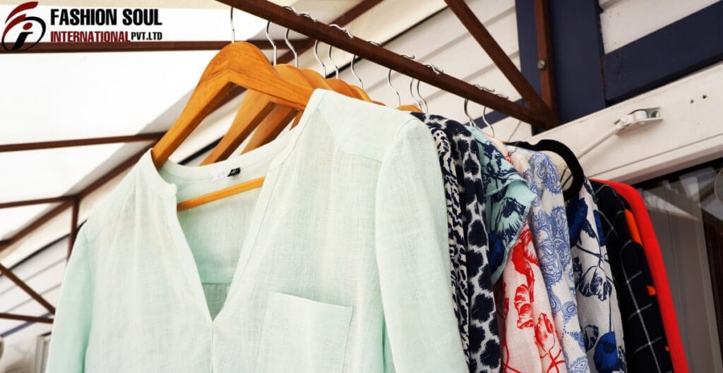 A row of hanging clothes including a white top and patterned scarves or fabrics, displayed on a rack inside a store or storage area.
