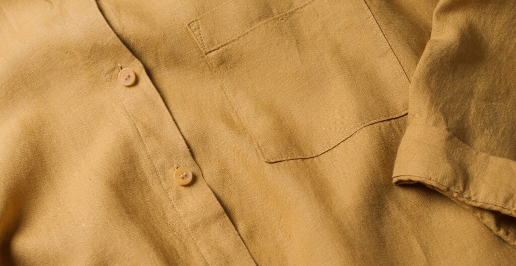 Close-up image of a light brown or tan button-up shirt with visible buttons and a chest pocket.