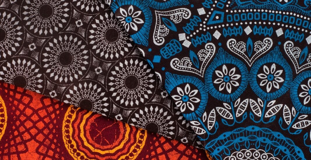 hree overlapping pieces of fabric with intricate, colorful patterns. The top fabric is black with white geometric designs, the middle fabric is blue with white and blue floral motifs, and the bottom fabric is red with orange and yellow circular patterns.