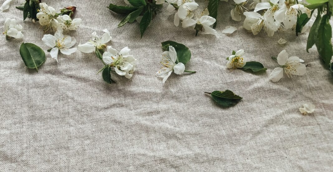 White flowers and green leaves scattered on a textured, light-colored fabric surface.