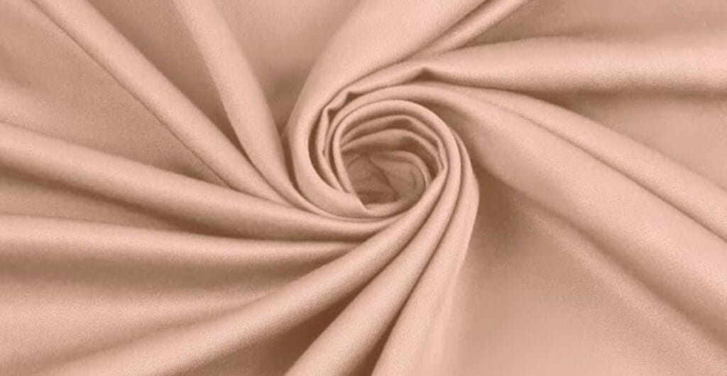 Close-up of light brown fabric with a smooth texture, gathered in a spiral pattern.