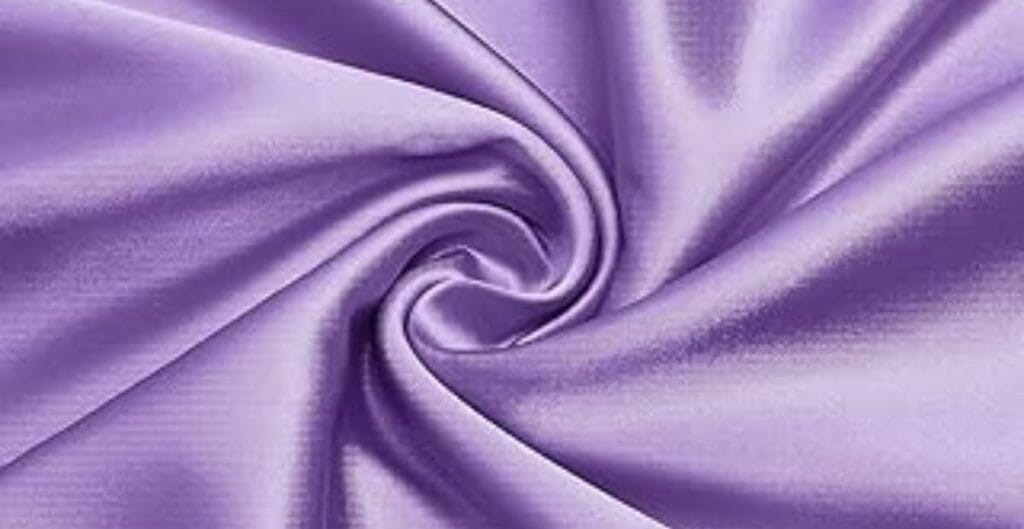 Close-up of lilac-colored satin fabric with a smooth, glossy texture, artistically twisted into a spiral pattern.
