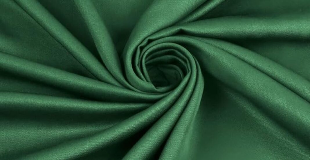 Close-up of emerald green fabric with a smooth, satiny texture, arranged in a spiral fold pattern.