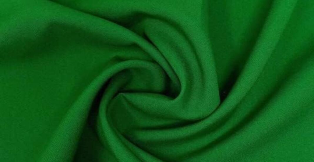 A close-up of a bright green fabric, gathered and twisted at the center to create soft folds and curves.