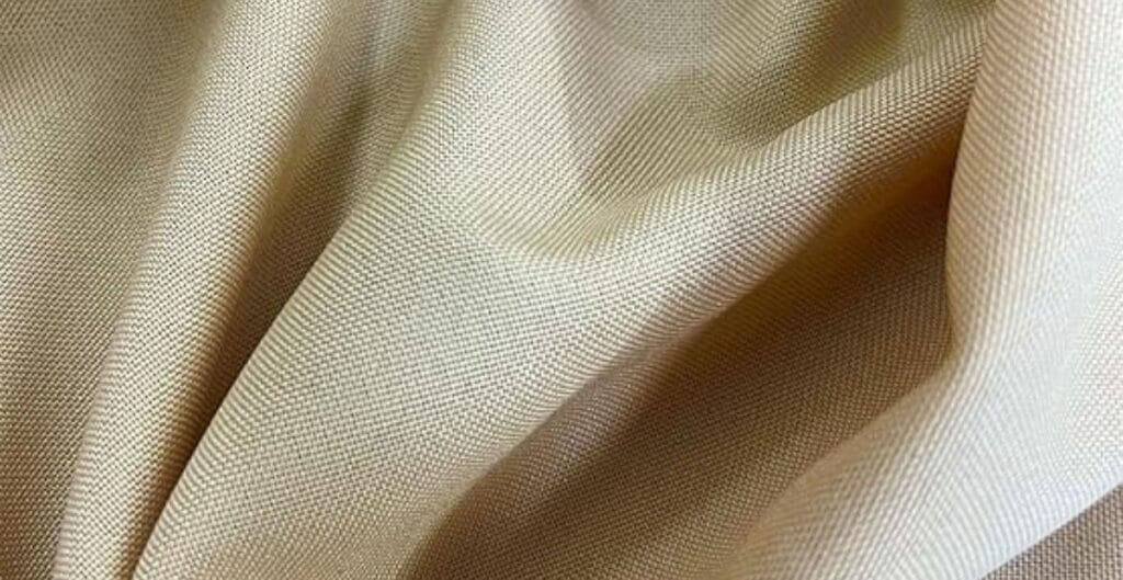 Close-up of beige-colored fabric with soft folds and a finely woven texture.