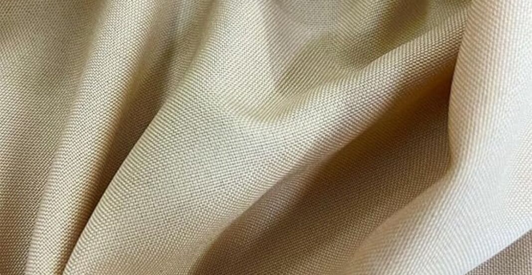 Close-up of beige-colored fabric with soft folds and a finely woven texture.