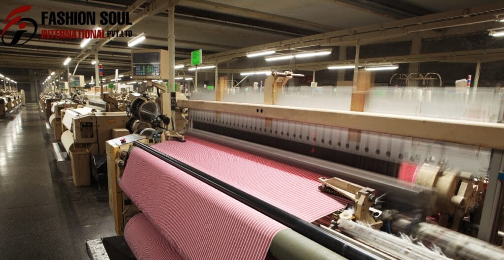 A textile manufacturing factory with a large industrial loom weaving pink and white striped fabric.