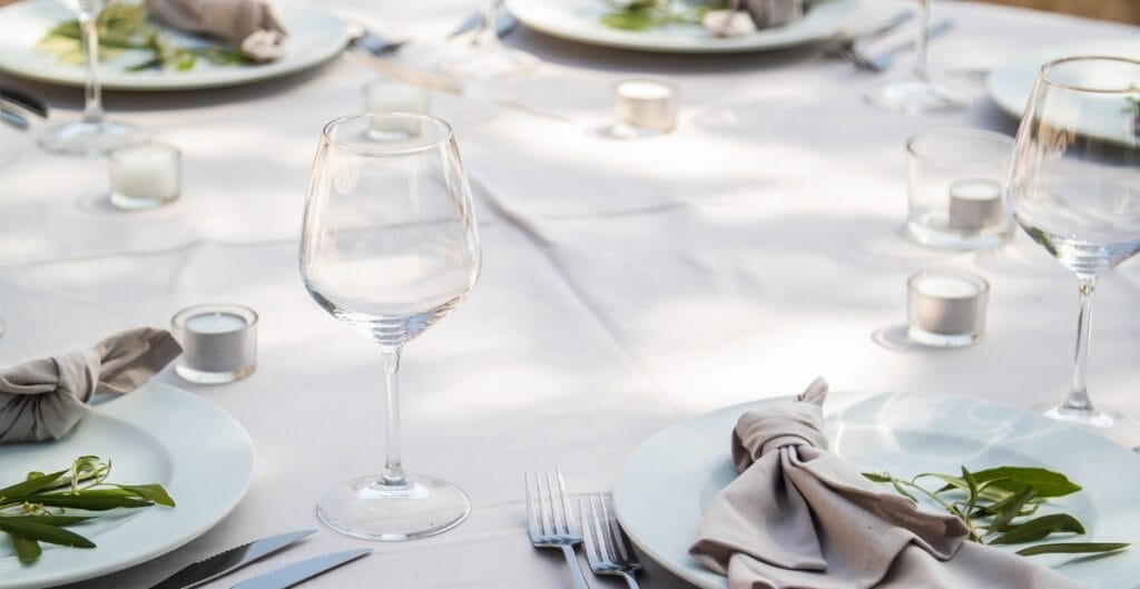 A neatly set dining table with white plates, cloth napkins, glassware, and small candles, prepared for a formal meal.