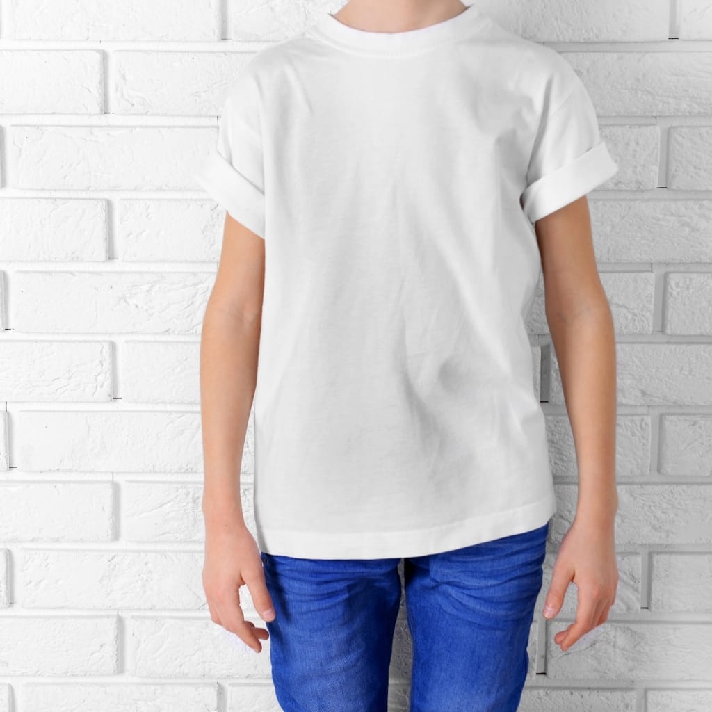 A person wearing a plain white short-sleeve T-shirt and bright blue jeans stands in front of a white brick wall.