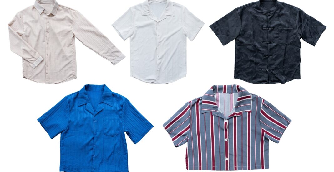 A collection of five diverse short-sleeve button-up shirts in various colors and patterns: a light pink striped shirt, a plain white shirt, a black shirt with a subtle pattern, a solid blue shirt with a ribbed texture, and a gray shirt with vertical red, white, and blue stripes.