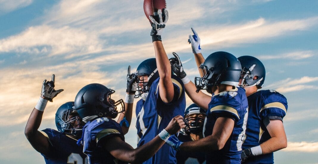 A group of football players in blue uniforms and helmets celebrating on the field under a cloudy sky.