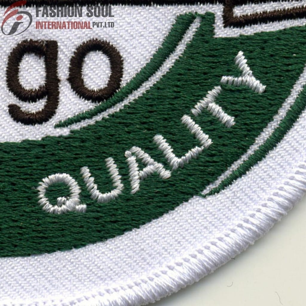  A close-up embroidered patch featuring the word "QUALIFIED" in white thread on a green background, with a white border. Part of a logo with "FASHION SOUL INTERNATIONAL PVT. LTD" is visible in the top left corner.