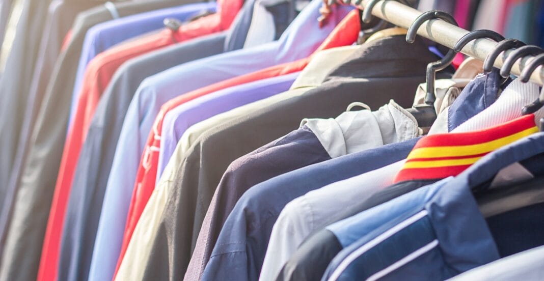 A variety of colorful jackets and shirts hanging on black plastic hangers on a clothing rack.
