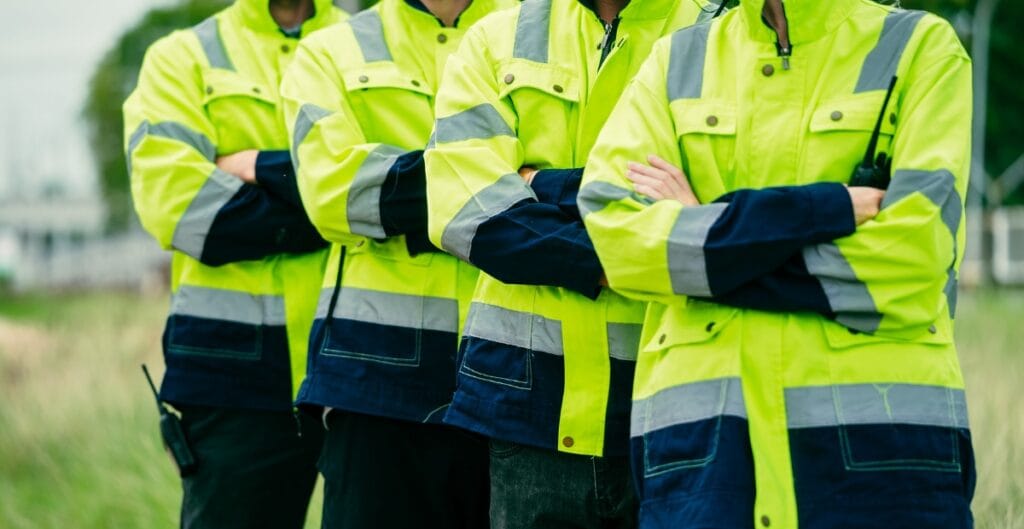 Four workers standing outdoors in high-visibility safety jackets with arms crossed.